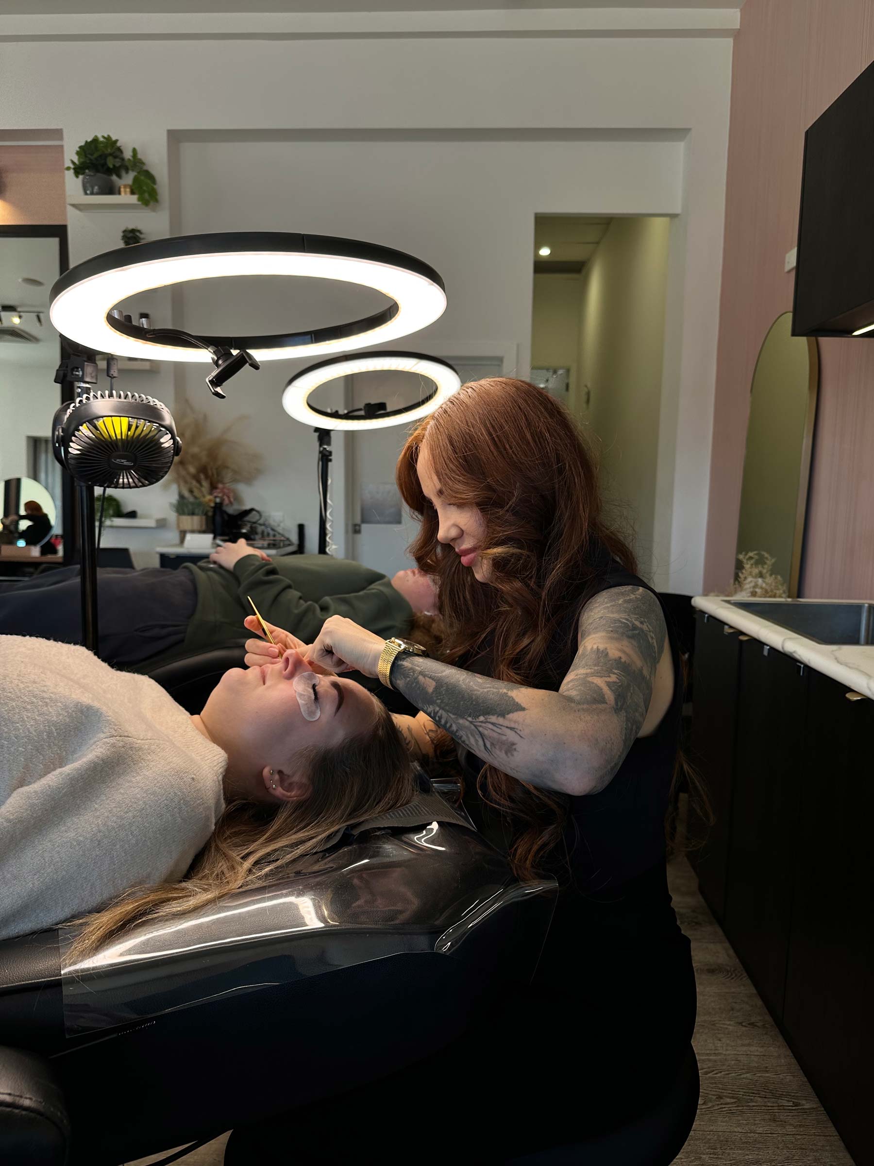 a woman applying makeup to another woman lying down in a beauty salon