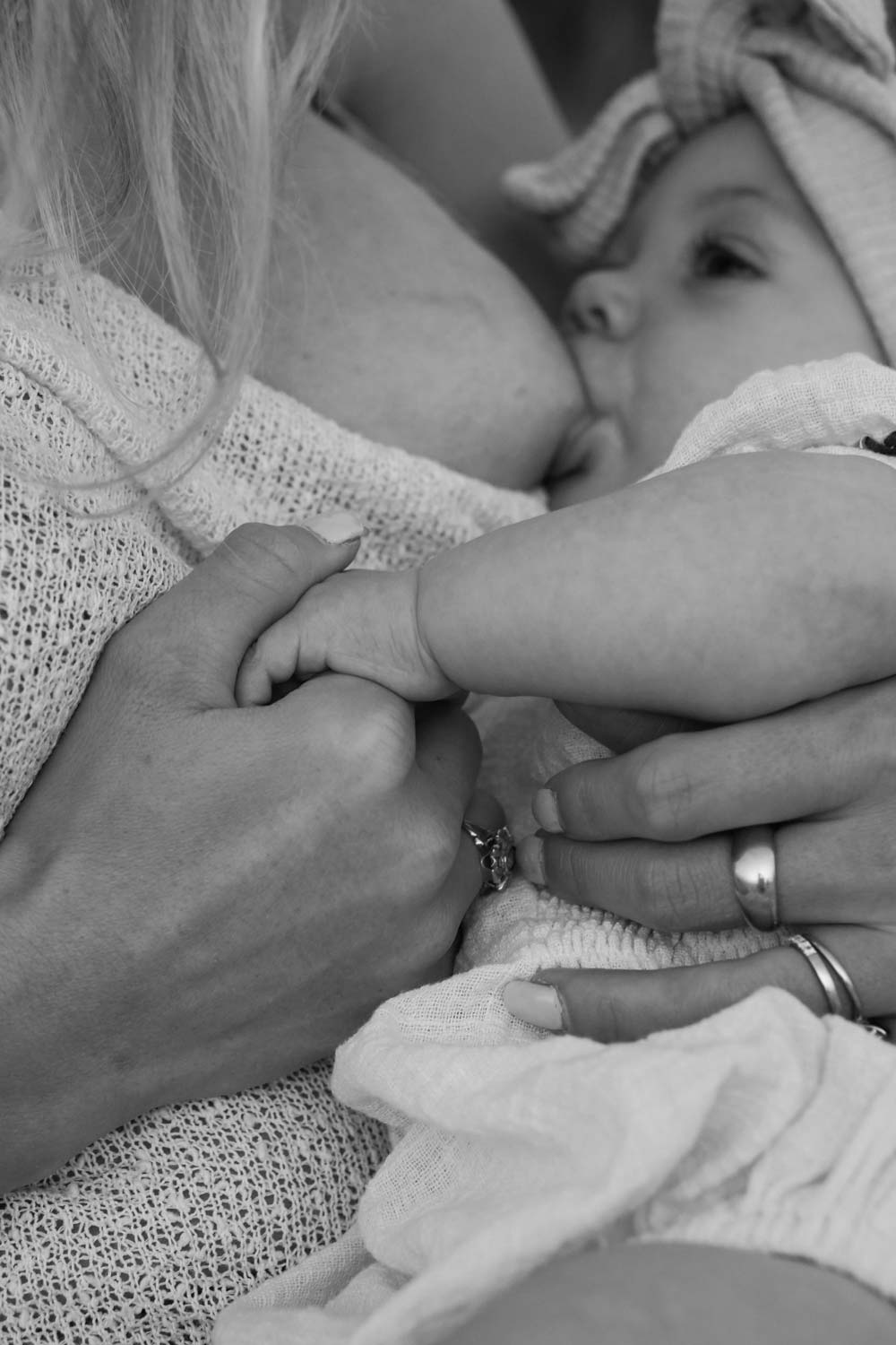 A mother holding her newborn's hand while breastfeeding