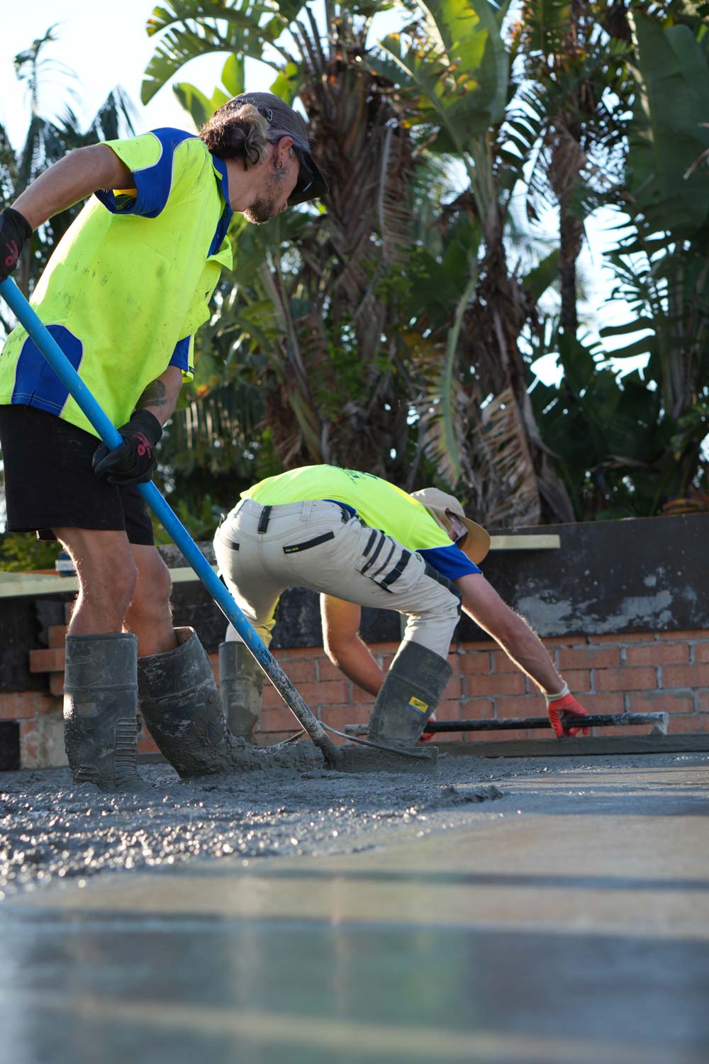 Two men screeding concrete with palms in the background