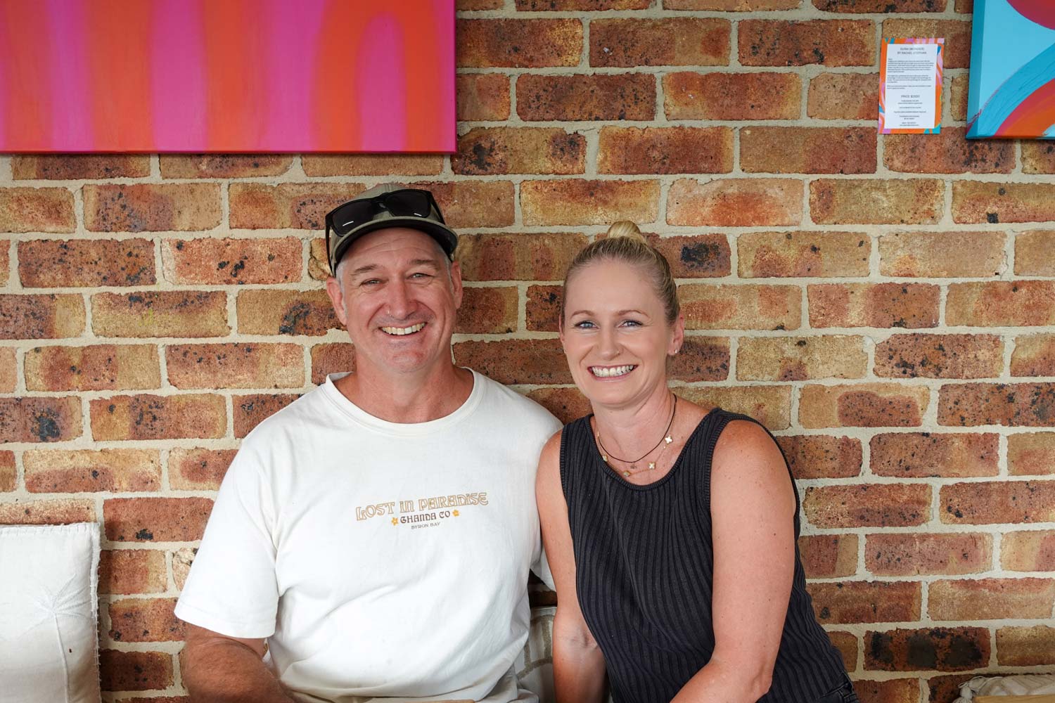 A couple smiling while sitting in front of a bric wall