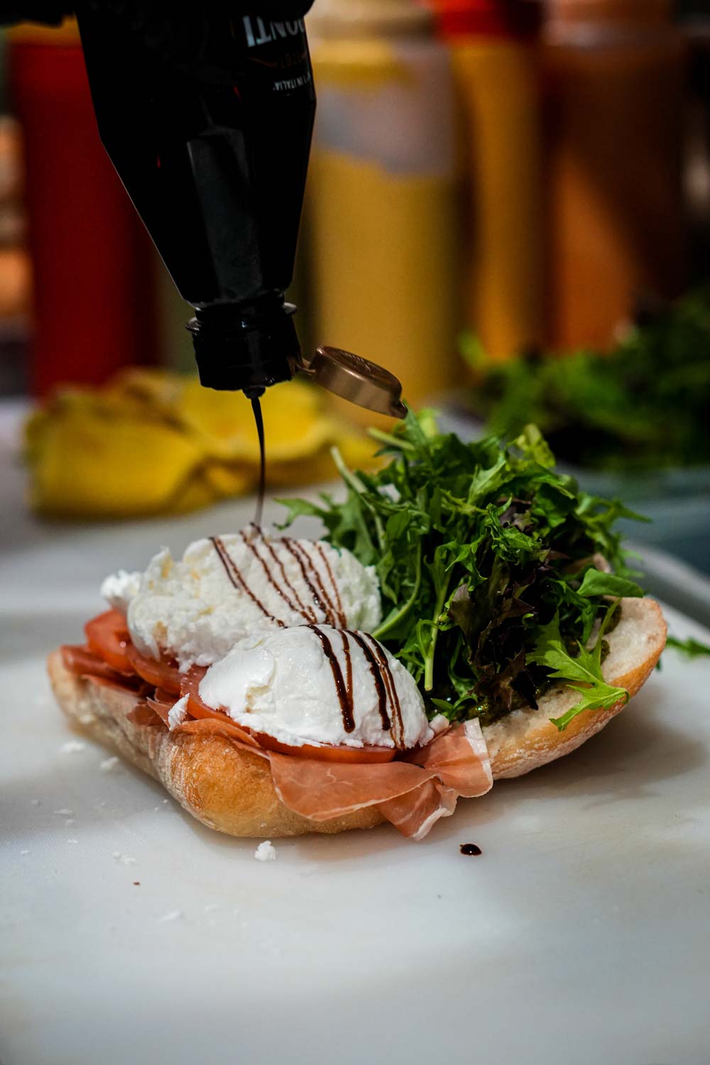 A panini with deli meats, lettuce and cheese being glazed with sauce